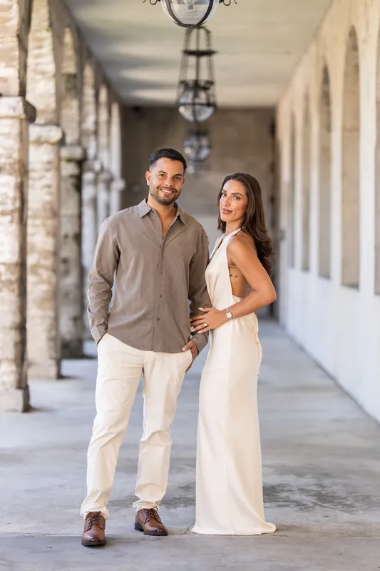 Beltran and Gabriela stroll together down the museum's portico, holding hands beneath ornamental iron lanterns.
