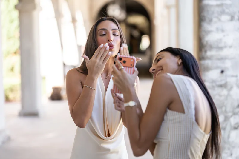 One person in white covers her mouth in surprise while another in cream laughs beside her under the museum's colonnade.