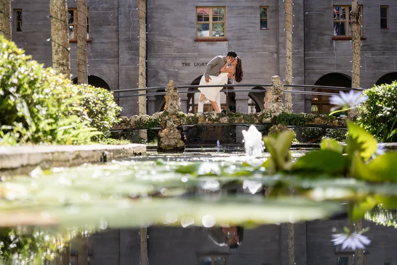 Two people embrace over a reflecting pool bordered by manicured hedges at the Lightner Museum Courtyard.