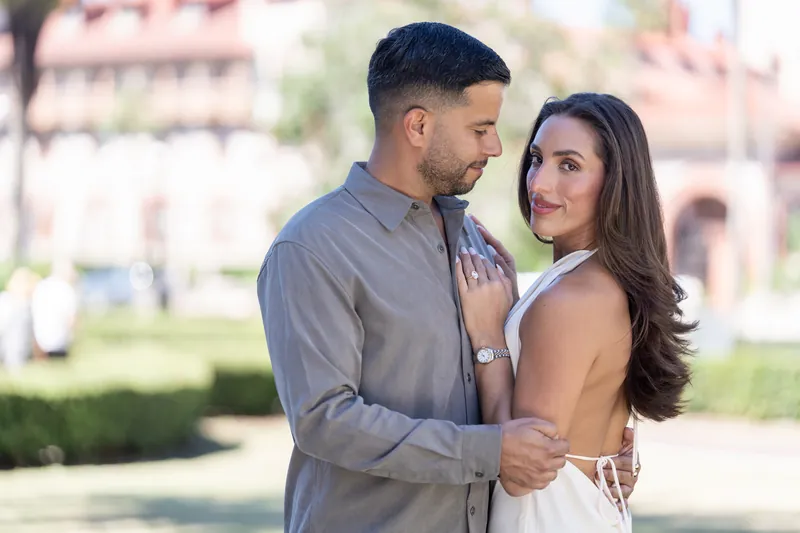 Beltran and Gabriela stand in the courtyard wearing casual attire, his arm around her shoulders as they look toward each other.