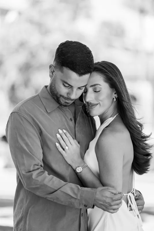 They embrace with foreheads nearly touching, captured in monochrome with blurred architectural elements in the background.