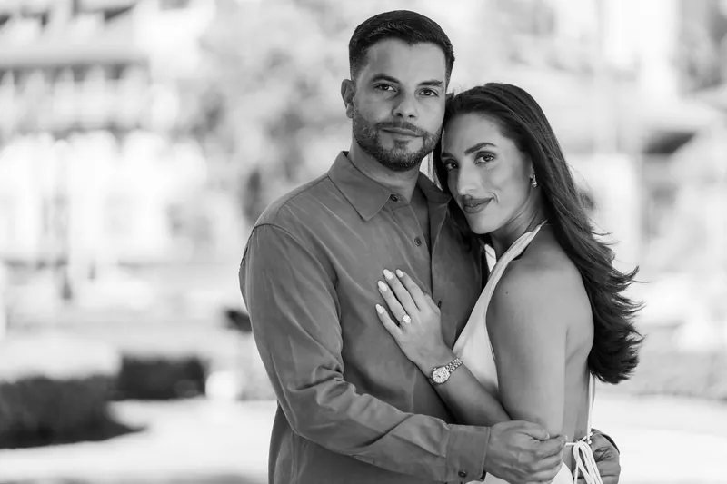 Beltran and Gabriela stand wrapped in each other's arms, gazing tenderly downward in a black and white portrait.