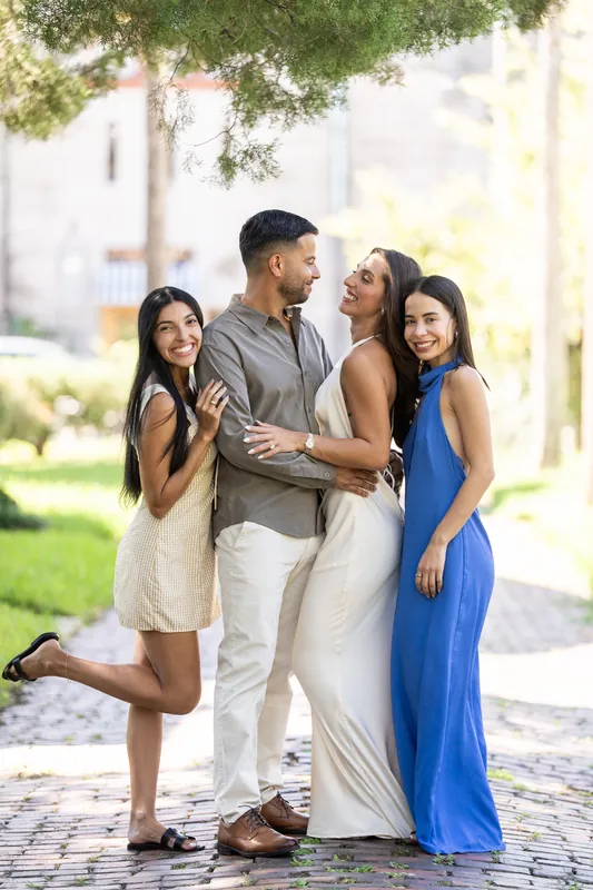 Two people stand with Beltran and Gabriela on the brick plaza, celebrating with the newly engaged couple beneath leafy trees.