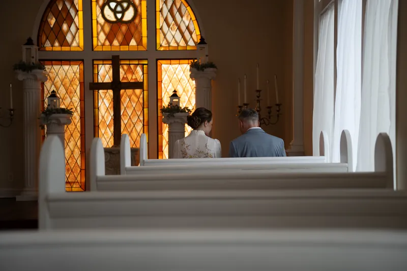 Couple seated in chapel pew facing golden stained glass windows