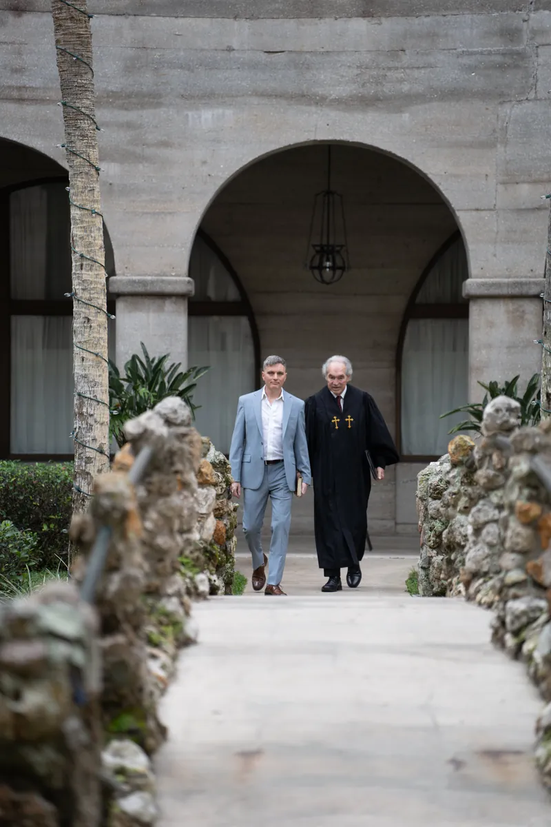 Groom walking with officiant through stone arches