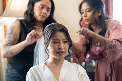 Bride getting hair styled by two women in indoor preparation room