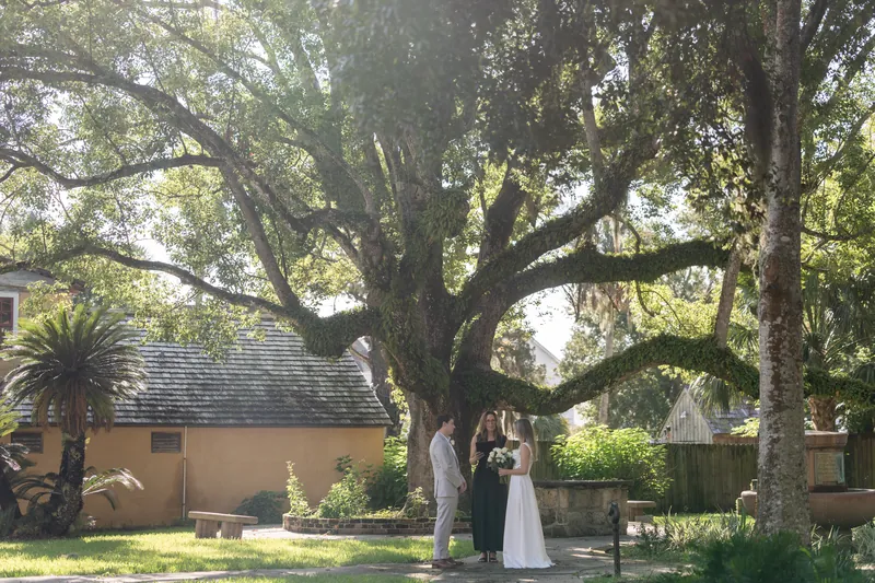 Blair and Devin stand together under a massive oak tree with Spanish moss at St. Francis Park, flanked by historic buildings.