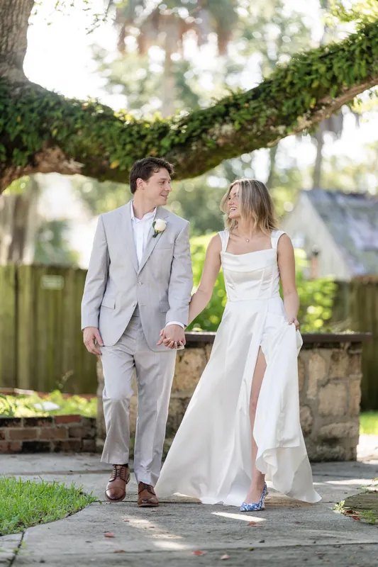 Devin and Blair hold hands walking beneath a sprawling oak, Blair's white dress flowing behind them.