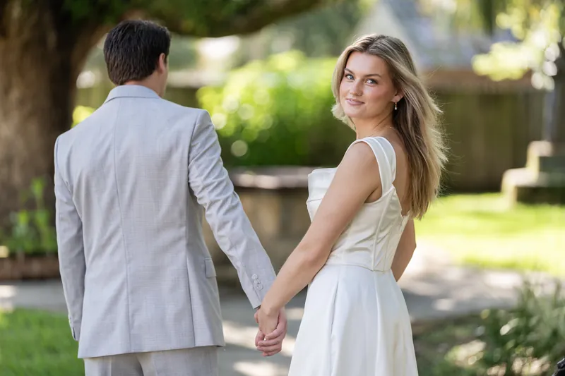 Devin and Blair hold hands under trees at St. Francis Park in their wedding attire.