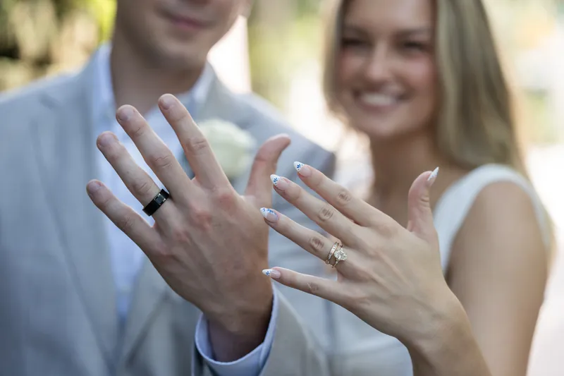 Blair and Devin display their wedding rings side by side, both smiling with hands raised toward the camera.