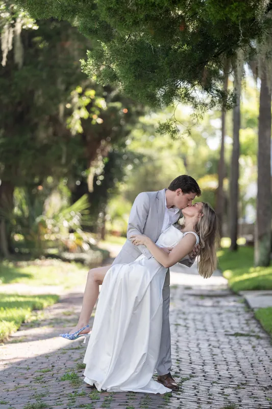 Devin dips Blair back for a kiss on the shaded brick walkway, framed by towering palms overhead.