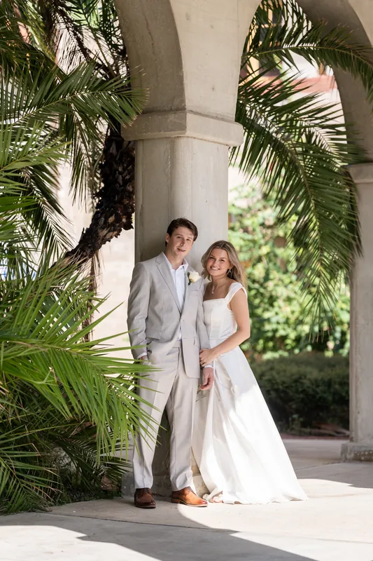 Under a columned archway at Lightner Museum Courtyard, Blair and Devin stand close together amid lush greenery.