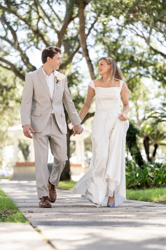 Hand in hand, Devin and Blair stroll down a sunlit brick path lined with mature oaks.