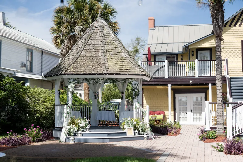 Bayfront Marin House's white gazebo with a peaked roof and floral arrangements sits on a brick patio, flanked by historic