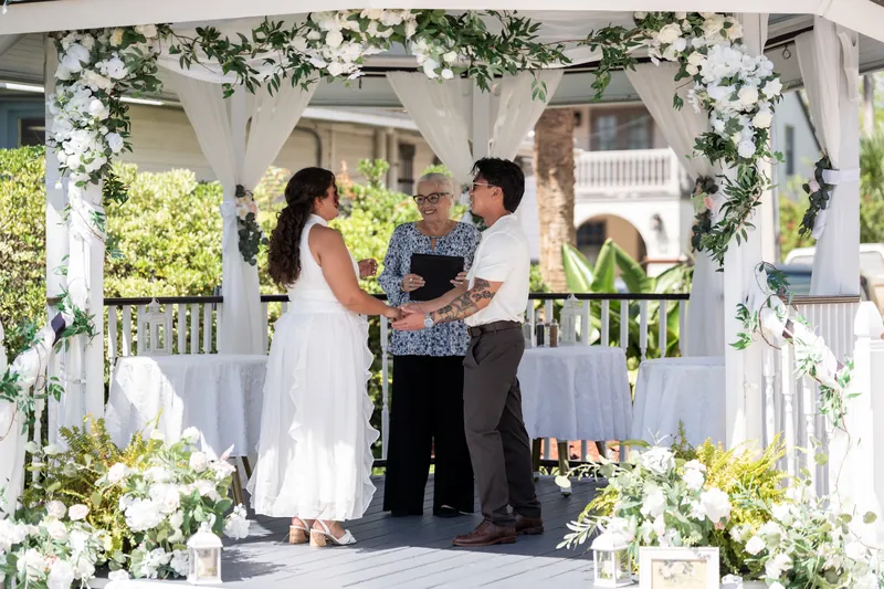 Blossom and Chris exchange vows beneath a white pergola draped with greenery at Bayfront Marin House, St. Augustine