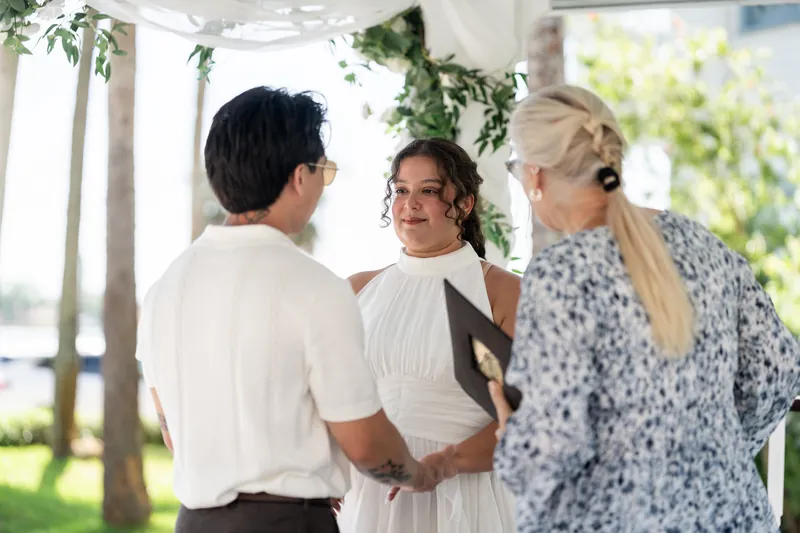 Chris, Blossom, and the officiant stand together under vine-covered beams at the indoor pavilion during the service.