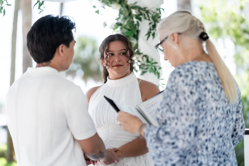 Blossom holds hands with Chris as the officiant reads vows beneath hanging greenery and natural light.