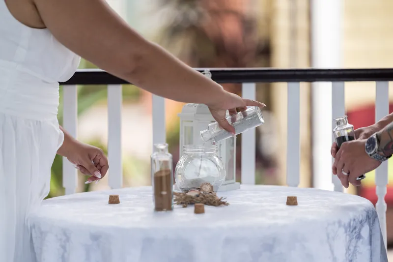 Hands arrange items on a white-draped table during the elopement ceremony.