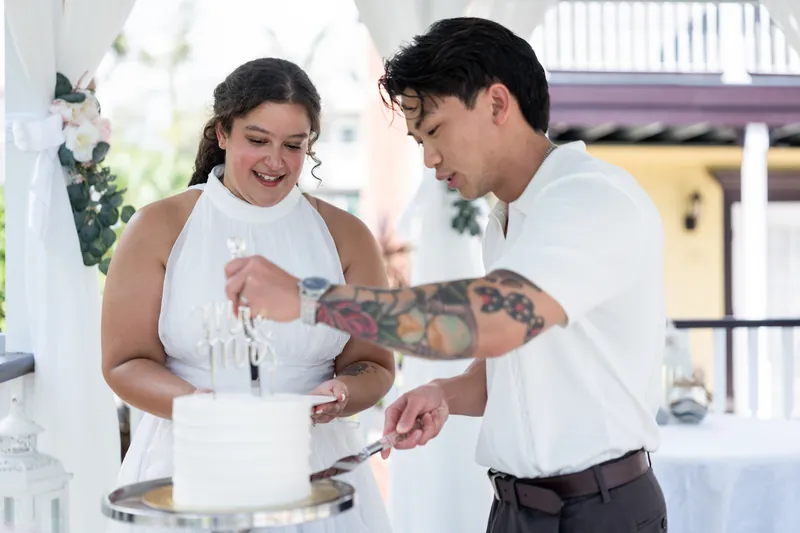 Blossom and Chris cut into their wedding cake together, both smiling as they hold the knife at Bayfront Marin House.