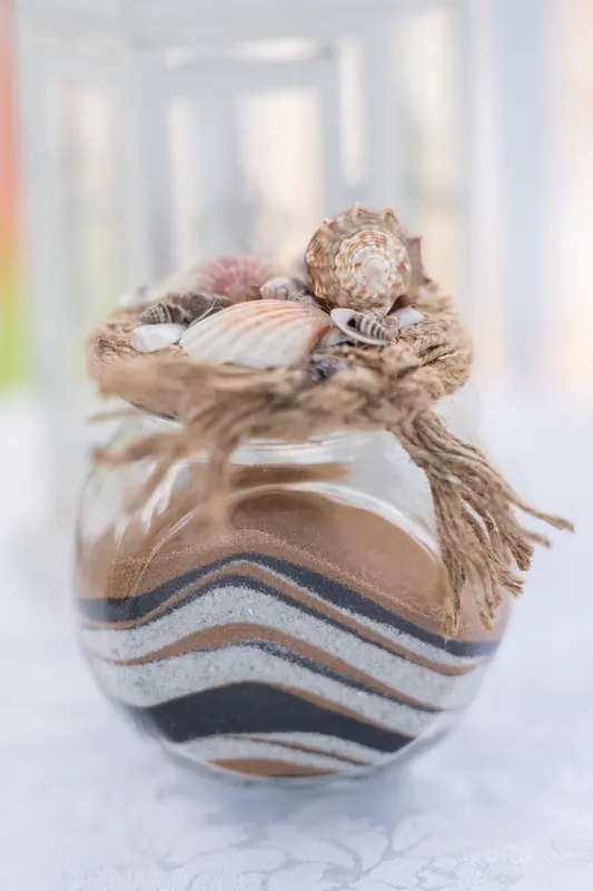 Close-up of a small woven ornament holding shells and twine, resting on a striped fabric surface with soft natural light.