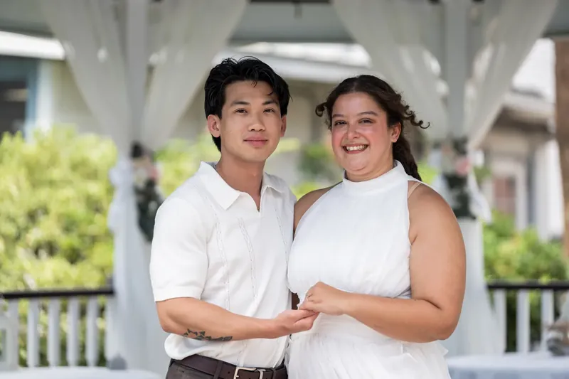 Blossom and Chris stand together under white pergola beams at Bayfront Marin House, both in white sleeveless tops.