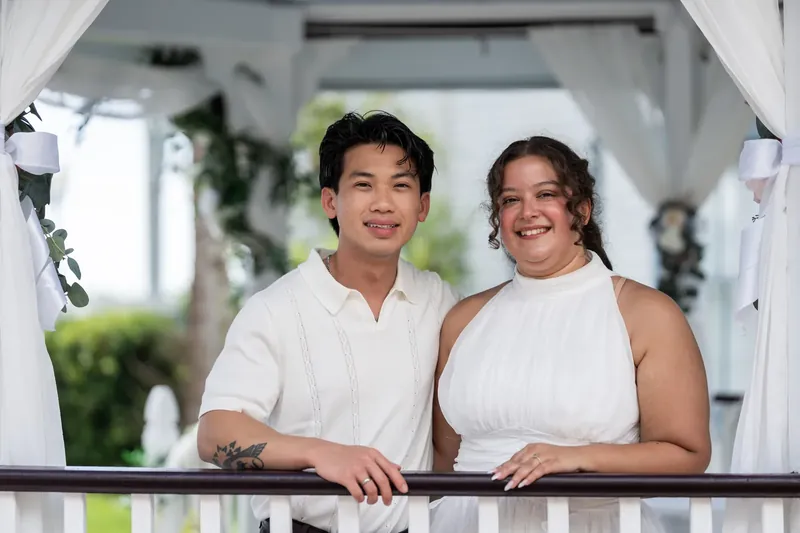 At the railing overlooking the grounds, they lean close together, both grinning widely in matching white attire.