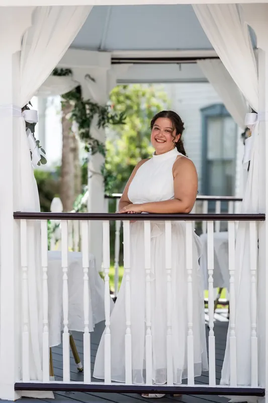 A person in a white sleeveless gown stands on the second-floor balcony, hands on the railing.