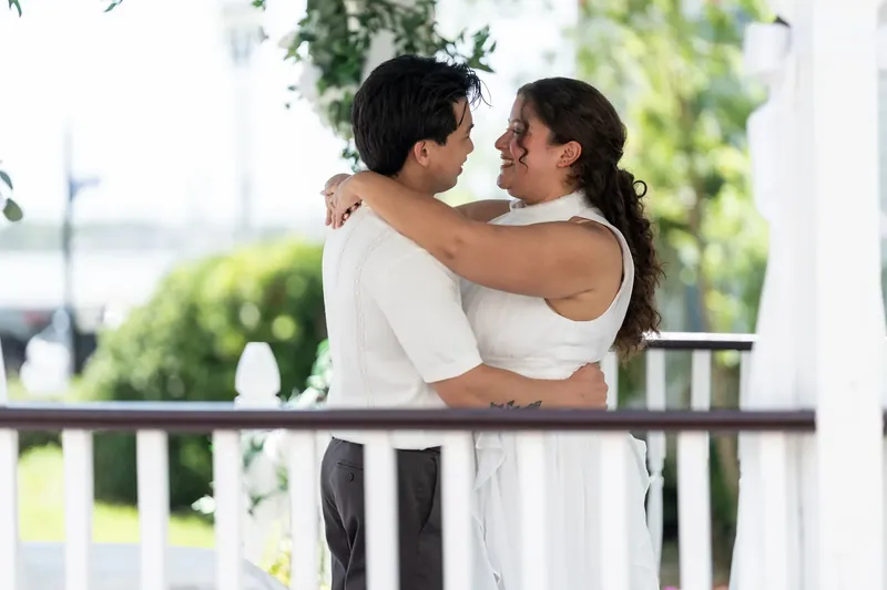 Blossom and Chris embrace on the porch at Bayfront Marin House, one in white and the other in a sleeveless top.