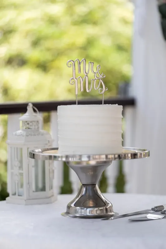 A white wedding cake topped with a "Mr. & Mrs." gold sign sits on a metallic stand overlooking the waterfront.
