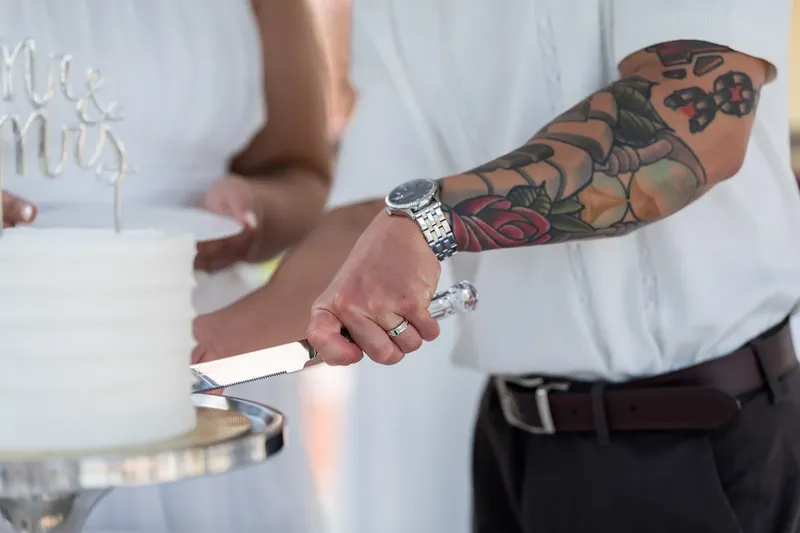 Tattooed arm and hand hold a ring while the other partner's hand rests nearby during the ring exchange.