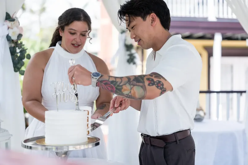 One partner slides a ring onto the other's finger as they stand together at the white cake table.
