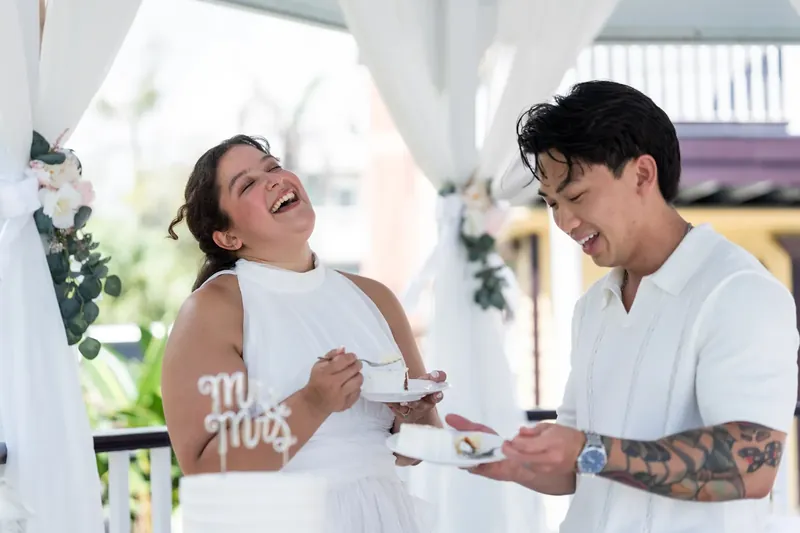 Both partners hold small plates of cake, laughing and looking at each other during their celebration.