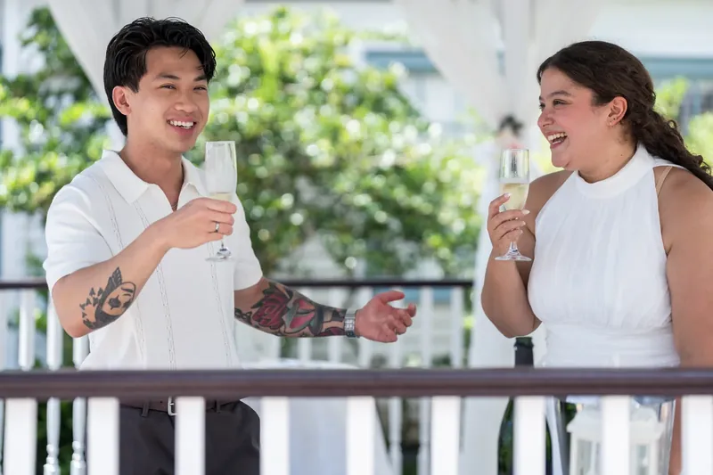 The couple raises their glasses in a toast, laughing together as afternoon light floods the venue.