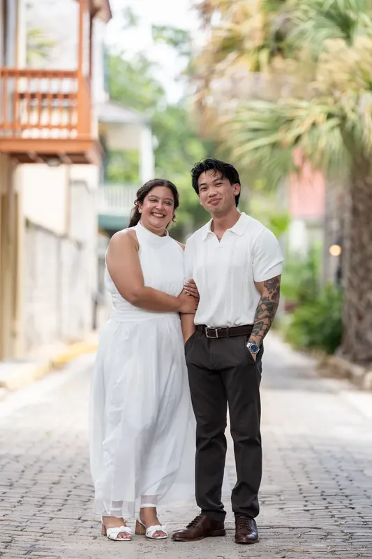 Blossom and Chris walk down a brick street lined with colonial architecture, holding each other close.
