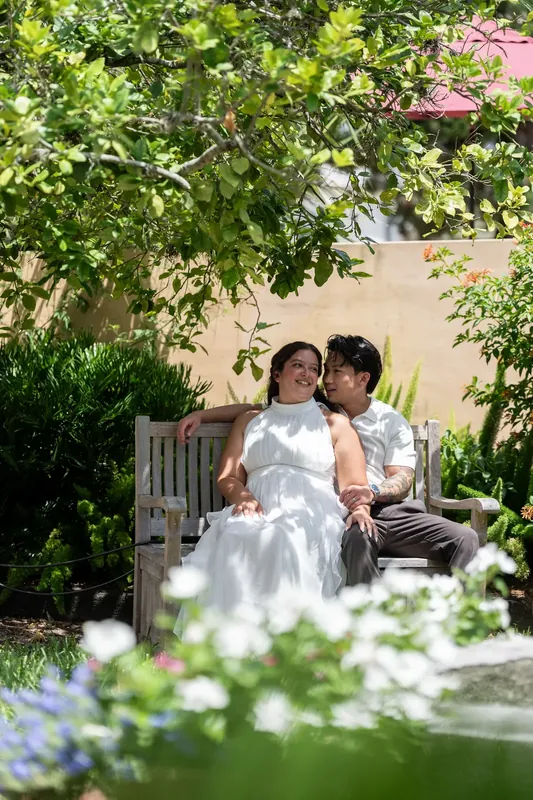 Two people sit on a wooden bench surrounded by flowering vines and greenery in Downtown St Augustine.