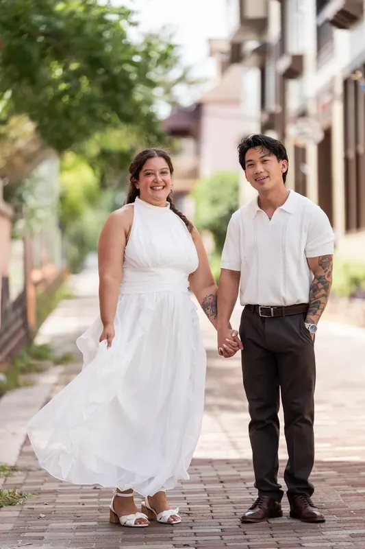 Blossom and Chris walk hand in hand down a brick street lined with historic buildings.
