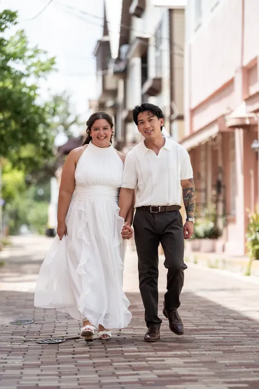 Two people walk away holding hands down a colonnade of historic brick buildings.