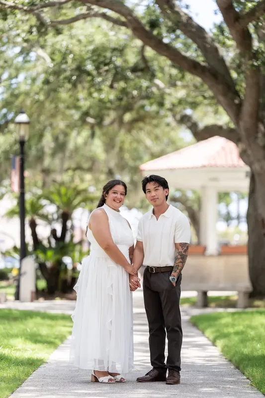 Blossom and Chris hold hands on a shaded brick path beneath towering oaks in downtown St. Augustine.