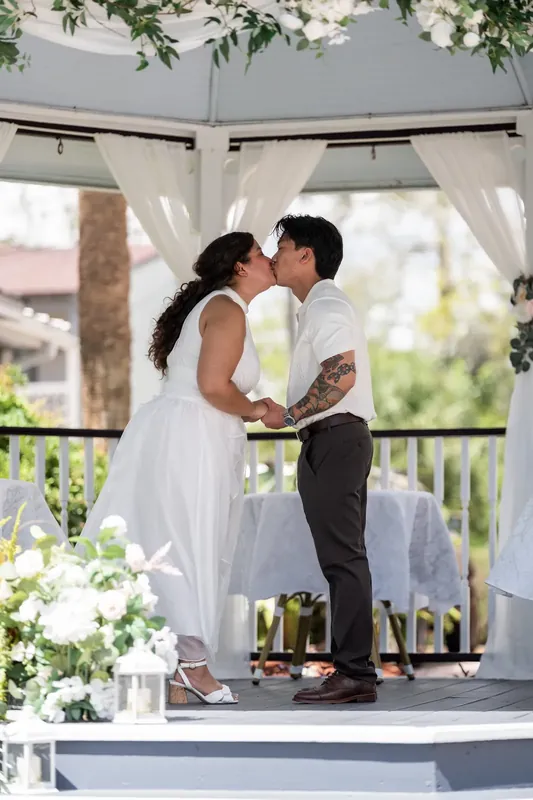Blossom faces two people under a decorated white pergola with greenery and flowers at Bayfront Marin House.