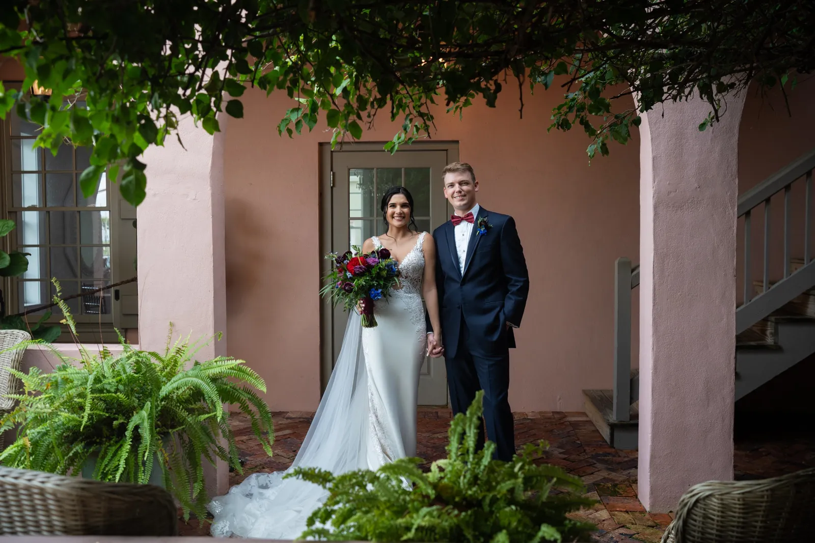 Bride and groom posing together in courtyard with flowering vines overhead