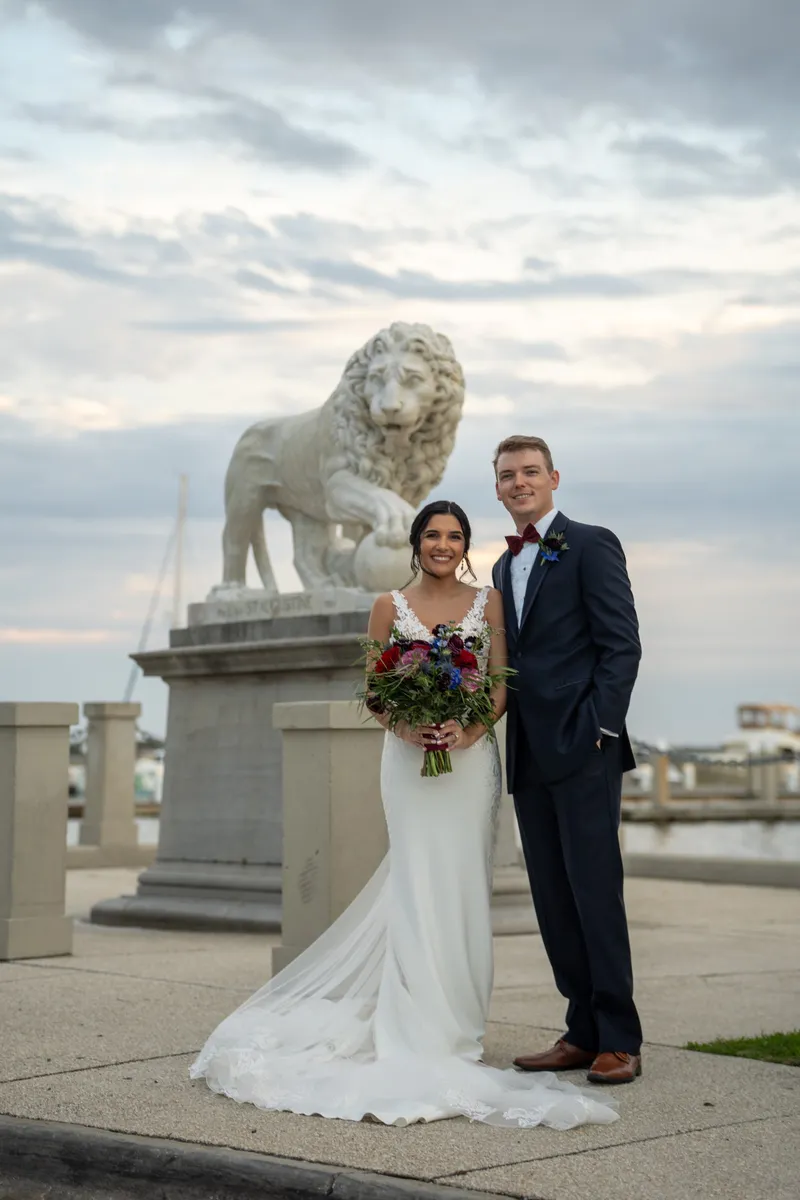 Bri and Nick pose by a stone lion statue at the Bridge of Lions with the skyline behind them.