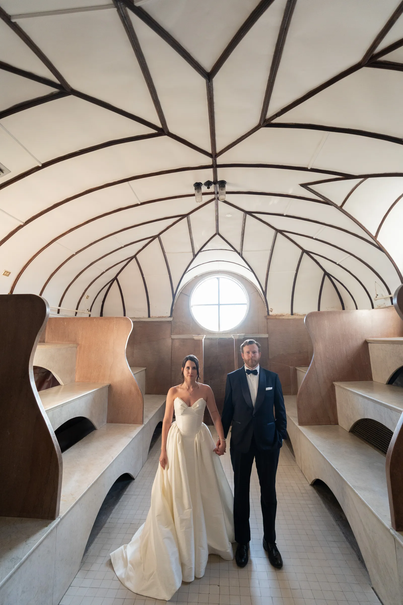 Bride and groom holding hands in modern architectural tunnel with geometric ceiling