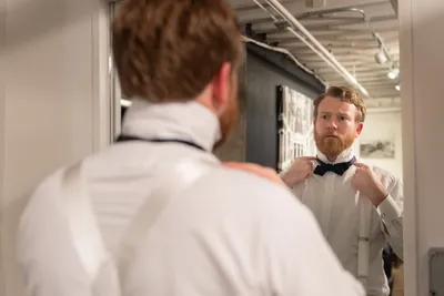 Man adjusting bow tie in mirror, formal white shirt preparation