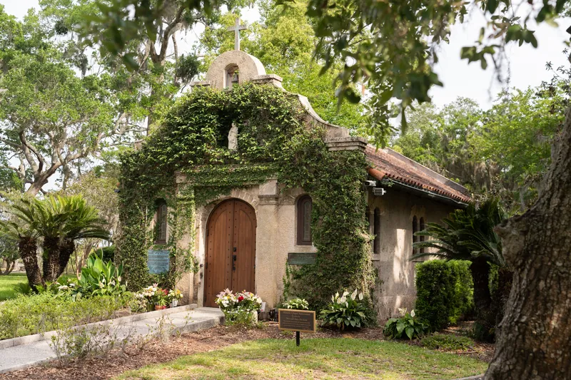Historic stone shrine with ivy-covered walls, wooden door, and palm trees surrounding the entrance at Mission Nombre de Dios.