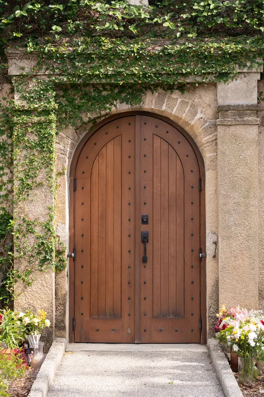Arched wooden door wrapped in climbing ivy with white flowers flanking the entrance to the historic shrine.