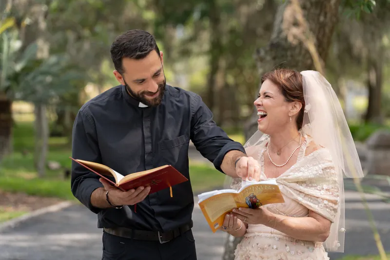 Dan and Bridgid hold open hymnals together, laughing during their ceremony beneath Spanish moss-draped trees.