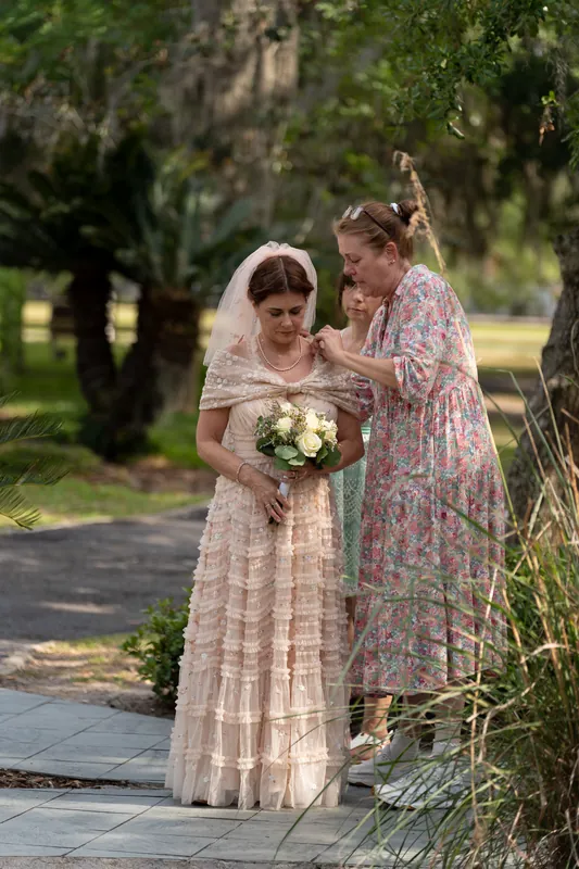 Bridgid in a lace dress and veil holds her white bouquet while standing with a family member under Spanish moss-draped oaks.