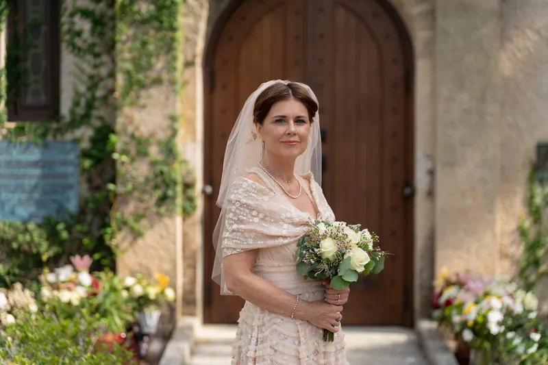 Bridgid poses alone before the ivy-covered stone chapel entrance, wearing an ornate lace gown and delicate veil.