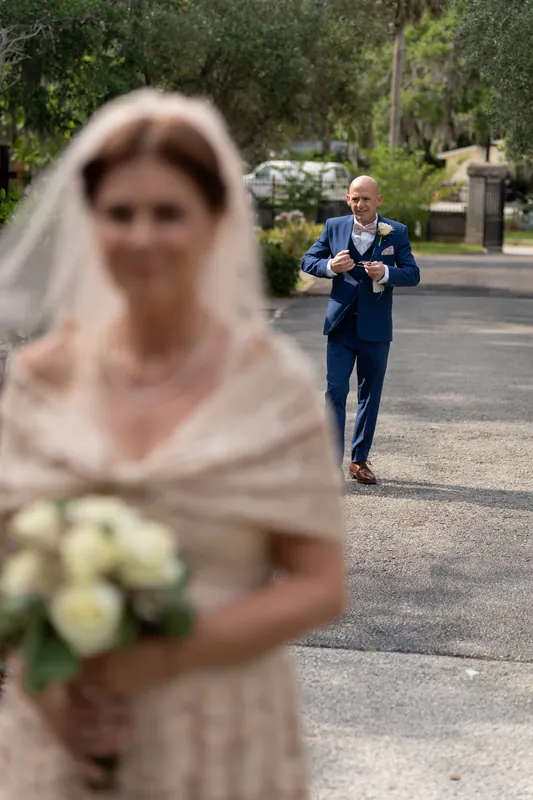 Dan approaches Bridgid down a tree-lined avenue, both in wedding attire with soft focus capturing the moment.