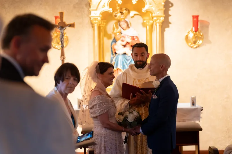 A priest in gold vestments officiates Bridgid and Dan's ceremony at the altar of the mission chapel.